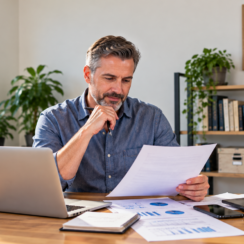 Middle-aged small business owner reviewing financing documents at his desk with a laptop and calculator.