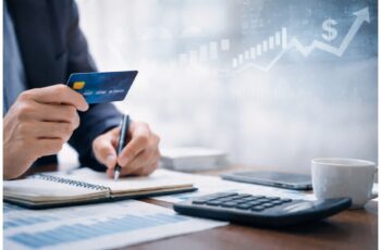 Business owner reviewing financial documents while holding a credit card and writing notes at a desk