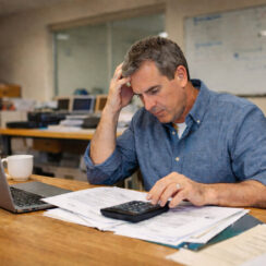 Stressed business owner reviewing bills and calculator showing warning signs of a business dependent on financing
