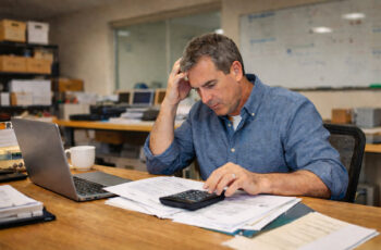 Stressed business owner reviewing bills and calculator showing warning signs of a business dependent on financing